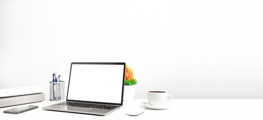 Blank white screen laptop on a white table in the office. Working concept using technology smartphones, notebook, coffee cup. Copy space on right for design or text, Closeup, Gray, and blur background