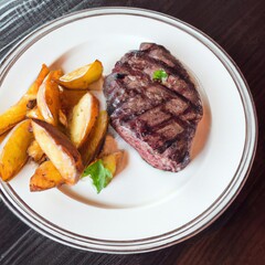 Grilled beef steak and potatoes on plate on the wooden table