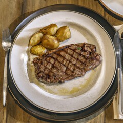 Grilled beef steak and potatoes on plate on the wooden table
