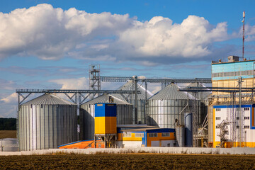 Fototapeta na wymiar Agricultural Silos. Storage and drying of grains, wheat, corn, soy, sunflower against the blue sky with white clouds.Storage of the crop