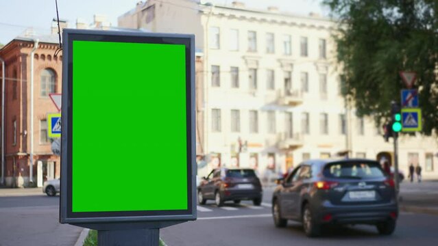 4k Green mockup billboard and cars drive in city street spbd. Vertical digital screen for advertising standing in center of modern town and transport moving on road in summer day. View of beautiful
