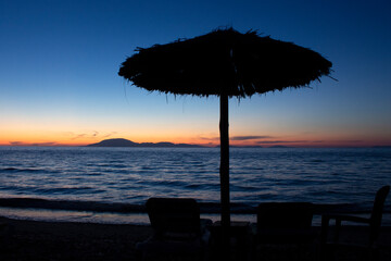 silhouette of umbrella and chairs  on the beach against sunset. summer in Greece