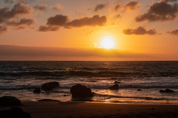Scenic view during sunset on the volcanic sand beach Playa del Ingles in Valle Gran Rey, La Gomera, Canary Islands, Spain, Europe. Sun beam reflection on water surface. Stones in the foreground