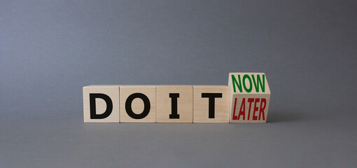Do it now or later symbol. Turned wooden cubes with words SDo it now or later. Beautiful grey background. Business concept. Copy space
