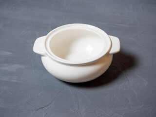 Close-up of an empty tureen made of white porcelain standing on a textured gray background. Dishes for food