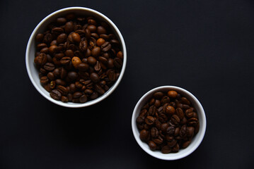 Fototapeta premium Delicious coffee beans in a ceramic white bowl on a black background. Coffee beans close-up in the dishes.