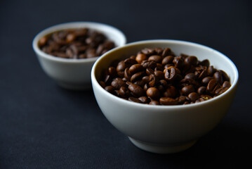 Delicious coffee beans in a ceramic white bowl on a black background. Coffee beans close-up in the dishes.