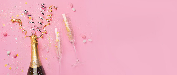 Champagne bottle with confetti on pink background.