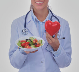 Portrait of a beautiful woman doctor holding a plate with fresh vegetables and red heart. Woman doctors.