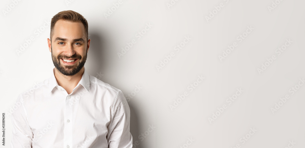 Wall mural Close-up of confident male employee in white collar shirt smiling at camera, standing self-assured against studio background