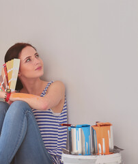 Woman choosing paint colour from swatch for new home sitting on wooden floor. Woman in the house