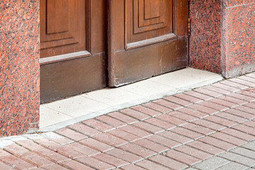 closed wooden entrance doors brown color with ceramic threshold, granite facade of building architecture near stone tile walkway close-up, nobody.