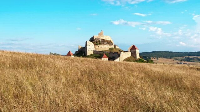 Aerial drone view of Rupea Fortress at sunset, Romania. Citadel located on a cliff, tourists, town, yellow field