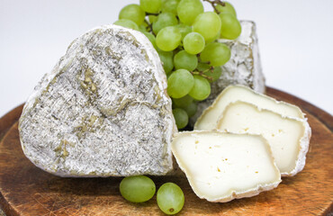 Assorted mouldy blue cheeses goat's milk on a wooden chopping board with green grapes. White background
