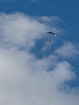 Paraglider flying in the blue cloudy sky.