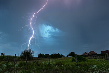 Powerful branched thunderbolt of lightning strikes down in an idyllic countryside