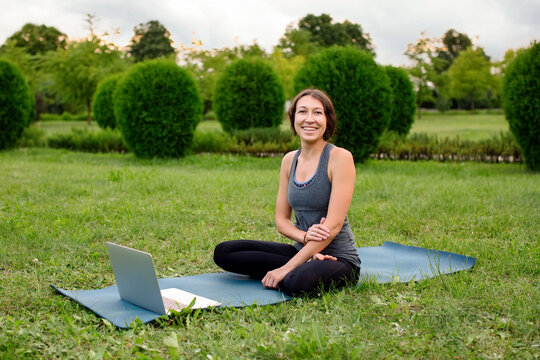 Young attractive women sitting at yoga class on fitness mat while watching fitness videos using laptop during video training. Concept of online classes, education distant app, high quality photo.
