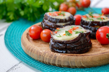 Eggplant baked with mozzarella cheese, tomatoes on a wooden plate, close-up.  Vegetarian food recipe