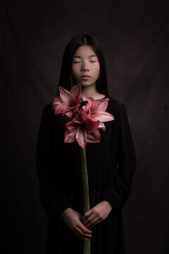 classic studio portrait of an asian woman in black dress holding a pink amaryllis flower