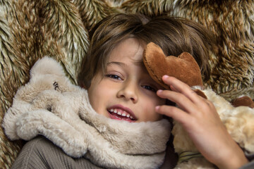 Close-up of an adorable smiling child looking at the camera on a brown blanket. Child inside the house on a cold winter day.  