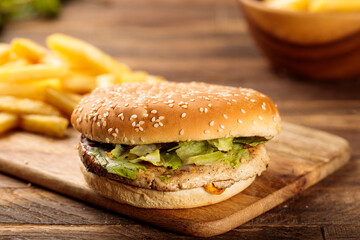 Chicken burger with french fries served in a cutting board isolated on wooden table background side view of fastfood