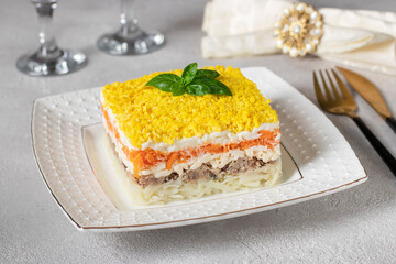 Traditional Russian puff salad Mimosa with canned fish, potatoes, cheese, carrots and eggs on gray background