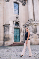 A young, blonde girl in a black blouse and sunglasses poses against the backdrop of an old courtyard in Lviv. Ukraine.