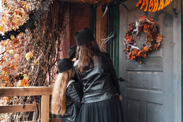 Scary girls, sisters, friends celebrating halloween. Playing treak or treat game on porch with garland. Bags with sweets in hands.Terrifying face skull makeup.Witch stylish costumes. Children's party