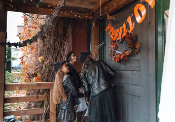 Scary girls, sisters, friends celebrating halloween. Playing treak or treat game on porch with garland. Bags with sweets in hands.Terrifying face skull makeup.Witch stylish costumes. Children's party