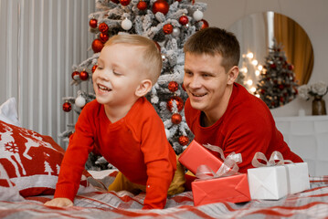 Happy dad tickle and have fun with excited small son near Christmas tree. Relax together, loving...