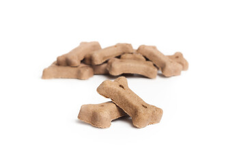 Dog biscuits in bone shapes with lamb. Isolated chewing bones in a pile. Small brown or beige pet food for snacking, training, enjoyment or dental hygiene. Selective focus. White background.