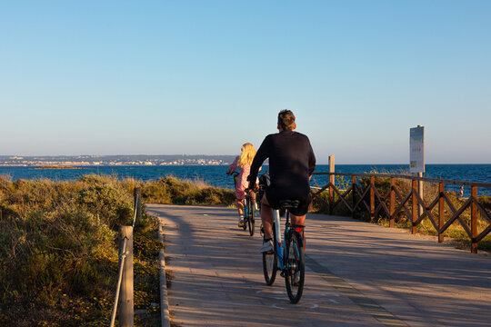 Pareja paseando en bicicleta al atardecer por un camino junto al mar en Palma de Mallorca (Islas Baleares, España). 