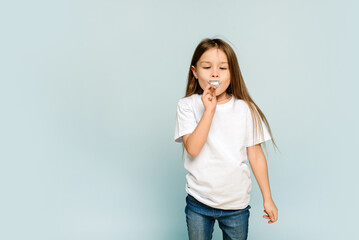 Pretty little kid girl in white t-shirt blowing in playing pipe on blue background. Copy space