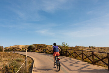Mujer ciclista subiendo una cuesta con su bicicleta en un camino junto al mar de Palma de Mallorca,...