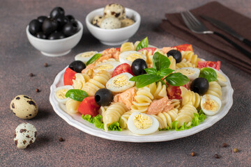 Canned salmon salad with pasta, cherry tomatoes, quail eggs, basil and black olives on brown background, Close-up