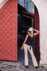 A young, blonde girl in a black blouse and sunglasses poses against the backdrop of an old courtyard in Lviv. Ukraine.