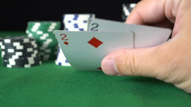 Poker game with a pair of duces betting all the poker chips. Close-up of a gambler hand is holding playing cards in poker club
