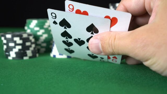 Poker game with a pair of nines betting all the poker chips. Close-up of a gambler hand is holding playing cards in poker club