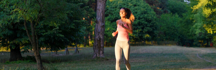 Young smiling fitness woman running in park in summer