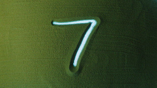 Hand drawing Number Seven 7 Symbol in the Green Sand. Male hand writes a number on the green sand with backlight. It is a series from 0 to 10. Top view 4k resolution