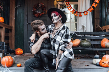 Scary love family couple man,woman celebrating halloween.Terrifying black skull half-face makeup,witch costumes.Stylish images,hat.Photoshoot,holiday party. Decorating of porch,pumpkin jack-o-lantern