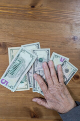 hands of an old woman lie on dollar bills on the table. View from above.