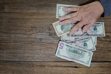 hands of an old woman lie on dollar bills on the table. View from above.