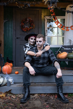 Scary love family couple man,woman celebrating halloween.Terrifying black skull half-face makeup,witch costumes.Stylish images,hat.Photoshoot,holiday party. Decorating of porch,pumpkin jack-o-lantern