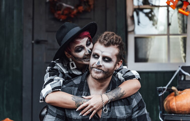 Scary love family couple man,woman celebrating halloween.Terrifying black skull half-face makeup,witch costumes.Stylish images,hat.Photoshoot,holiday party. Decorating of porch,pumpkin jack-o-lantern