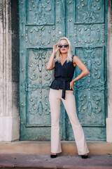 A young, blonde girl in a black blouse and sunglasses poses against the backdrop of an old courtyard in Lviv. Ukraine.