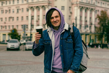 Hipster man with dreadlocks drinking hot coffee on street. Young male in warm clothes drinking hot beverage