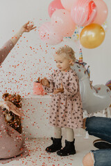 Little girl on her birthday. Little girl near cake, toys and confetti.