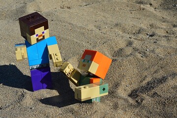 Naklejka premium LEGO Minecraft action figure of Steve in blue shirt helping his female friend Alex from shifty sand pit. Summer afternoon sunshine. 