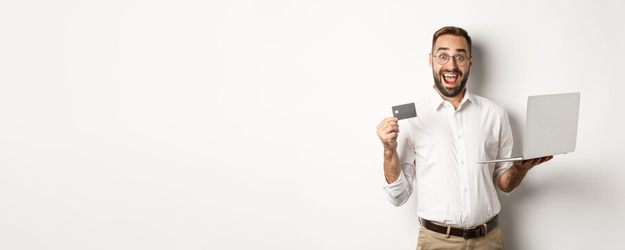 Online shopping. Handsome man showing credit card and using laptop to order in internet, standing over white background